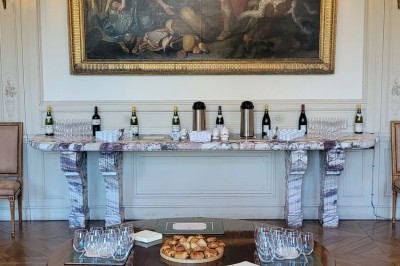 Salon lumineux avec parquet, mobilier classique, table ronde dressée au centre et lustre en cristal au plafond.