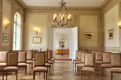 Salon lumineux avec parquet, mobilier classique, table ronde dressée au centre et lustre en cristal au plafond.