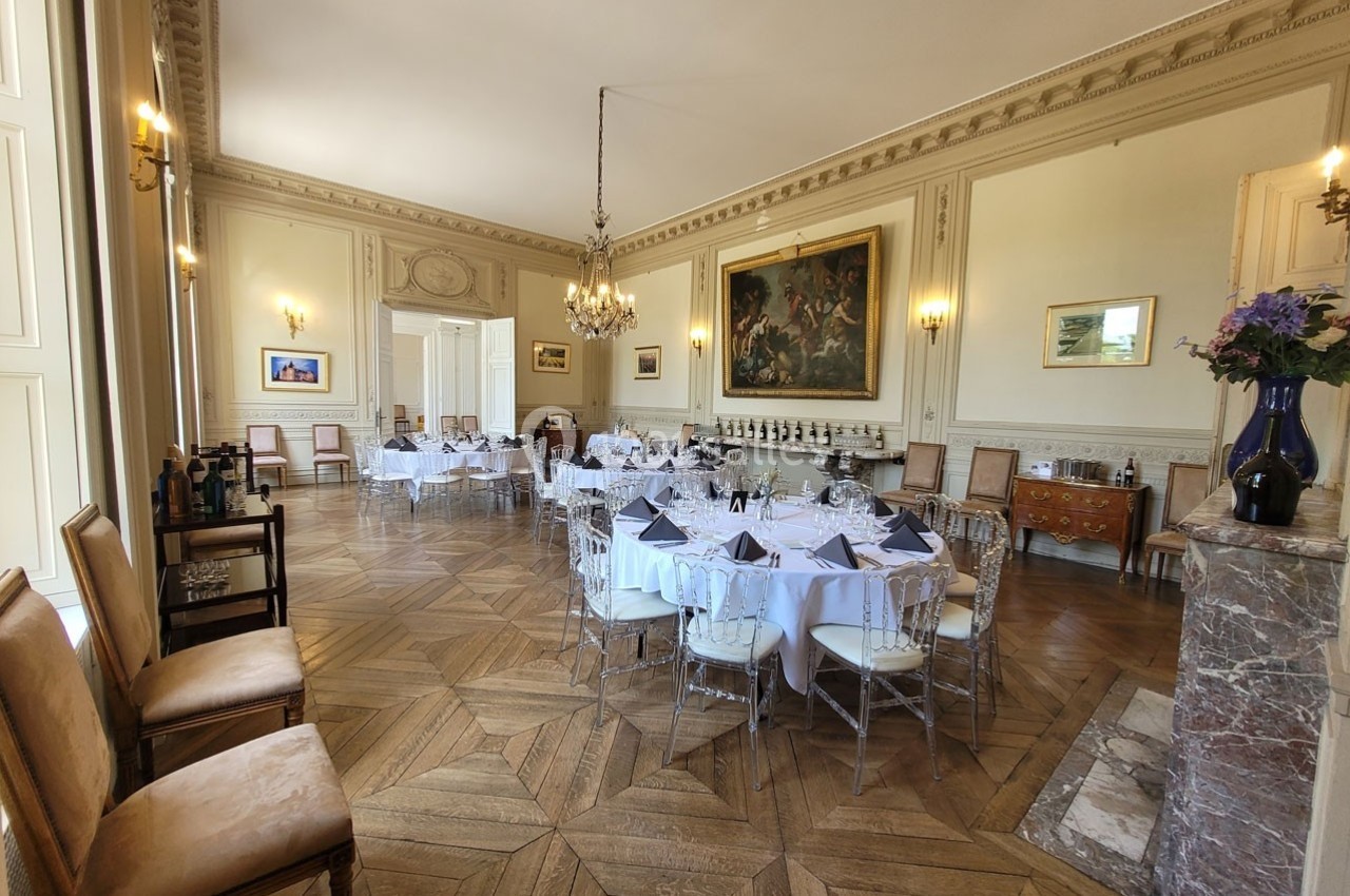 Salle élégante avec parquet en bois, tables rondes dressées, chandeliers et décoration classique.