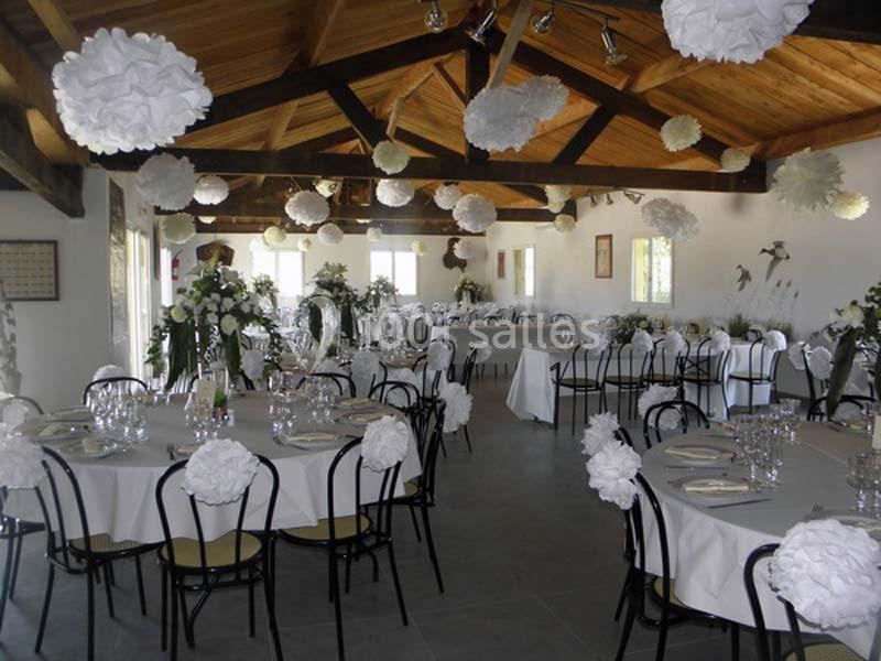 Salle de réception décorée avec des tables dressées, chaises noires et ornements blancs suspendus au plafond.