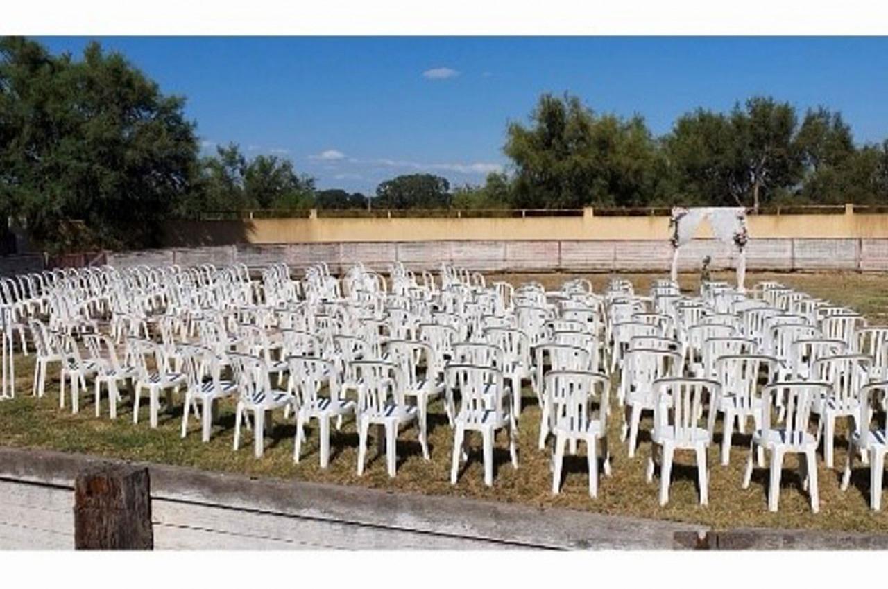 Chaises blanches disposées en rangées sur une pelouse, face à une arche décorée pour un événement en extérieur.