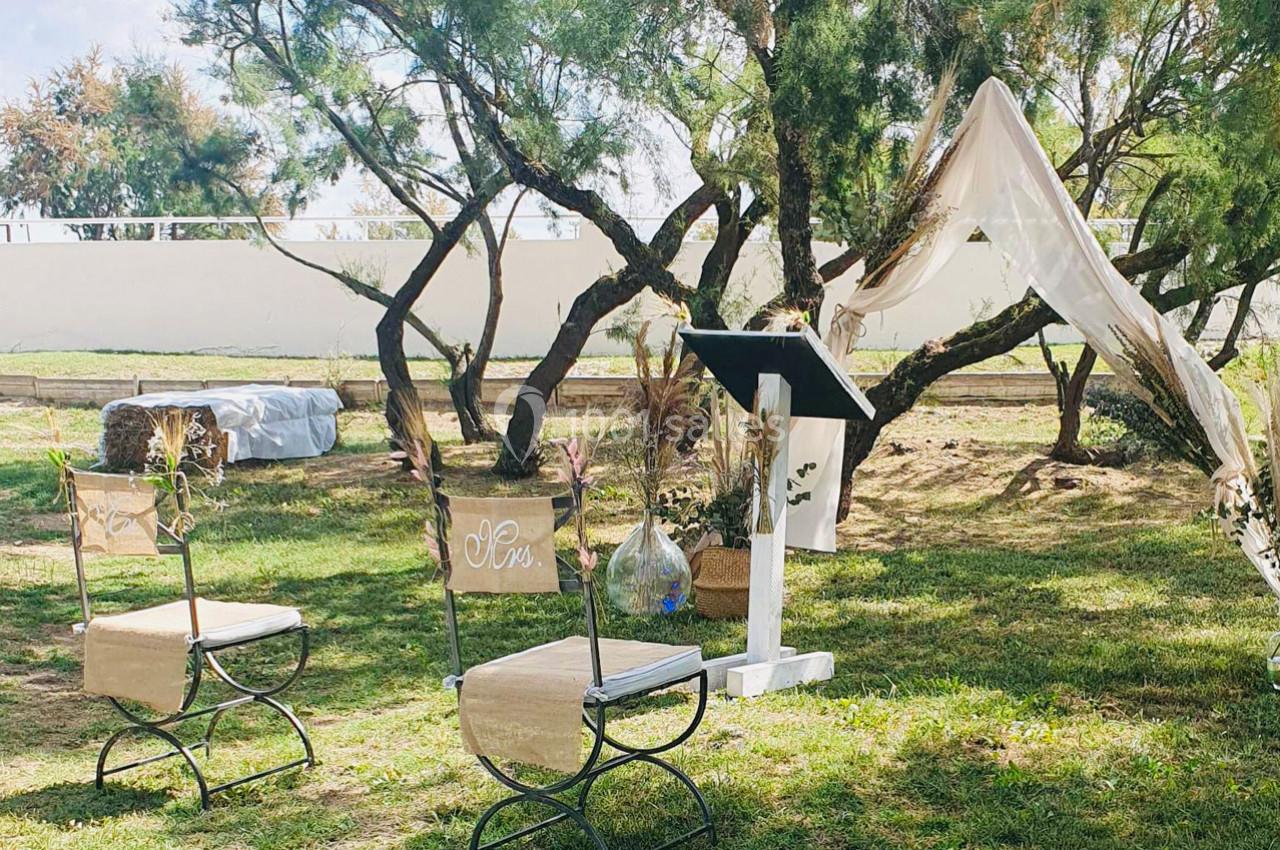 Chaises décorées et pupitre installés en extérieur sous des arbres, avec un voile suspendu en arrière-plan.