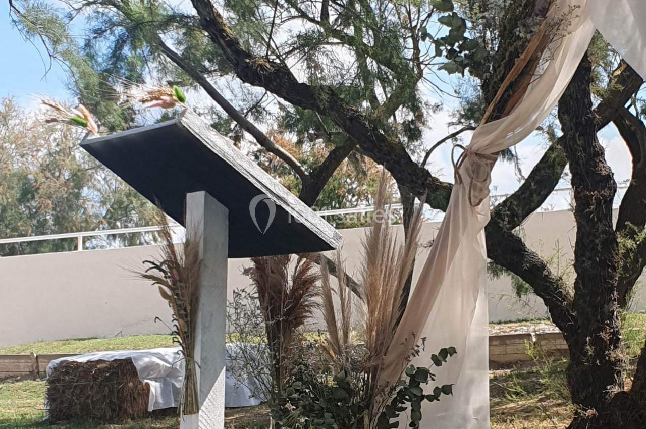 Un pupitre en bois décoré de fleurs séchées, placé en extérieur près d'un arbre avec des voilages suspendus.