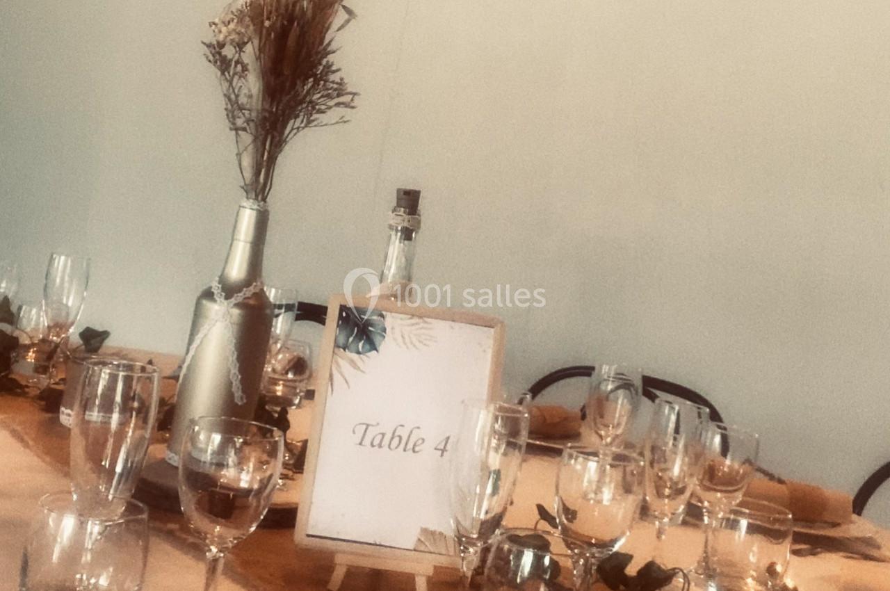 Table décorée avec des verres, une bouteille, un centre de table floral et un panneau indiquant ’Table 4’.