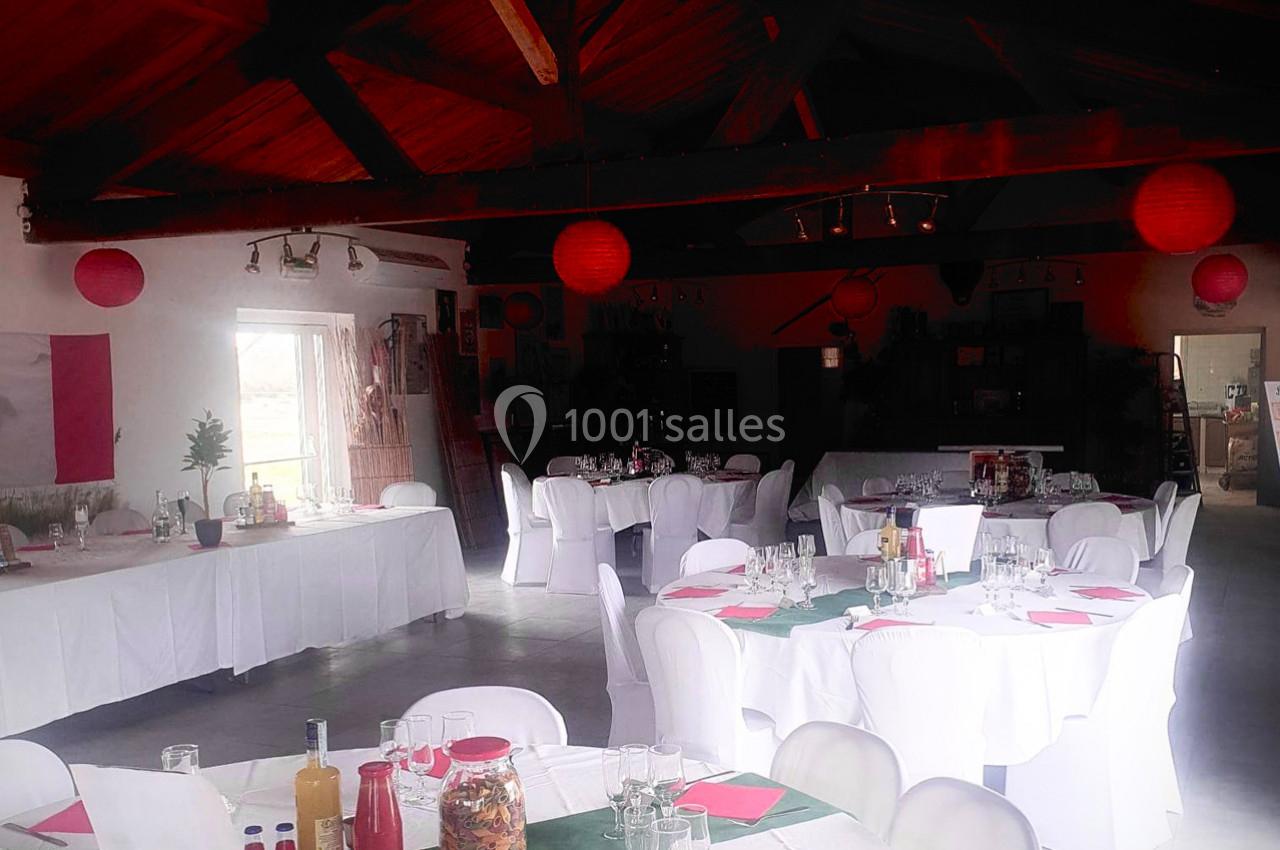 Salle de réception décorée avec des tables rondes dressées, nappes blanches et lanternes rouges suspendues.