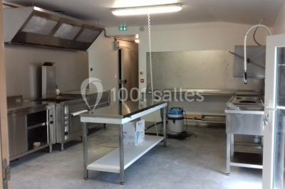 Chemin gravillonné bordé de barrières en bois menant à un bâtiment en pierre entouré de verdure.