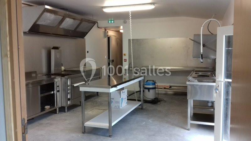 Cuisine professionnelle équipée avec plans de travail en inox, appareils de cuisson, hotte et évier industriel.