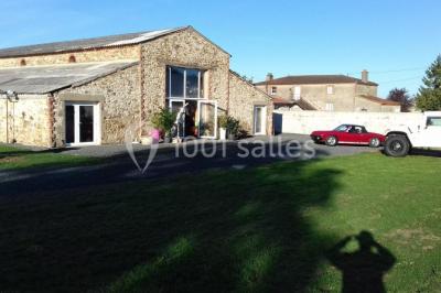 Chemin gravillonné bordé de barrières en bois menant à un bâtiment en pierre entouré de verdure.