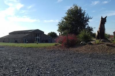 Chemin gravillonné bordé de barrières en bois menant à un bâtiment en pierre entouré de verdure.