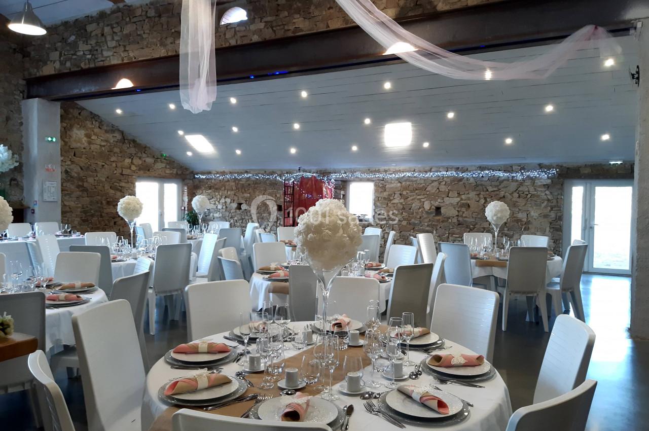 Salle de réception décorée avec des tables rondes dressées, nappes blanches et centres de table fleuris.