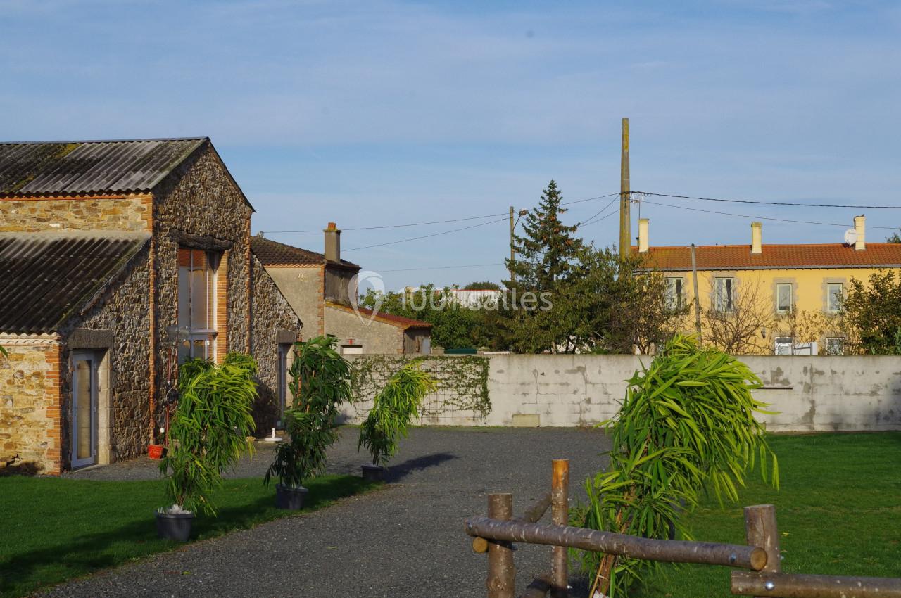 Cour extérieure avec des bâtiments en pierre, des plantes en pot et une clôture en bois, sous un ciel dégagé.