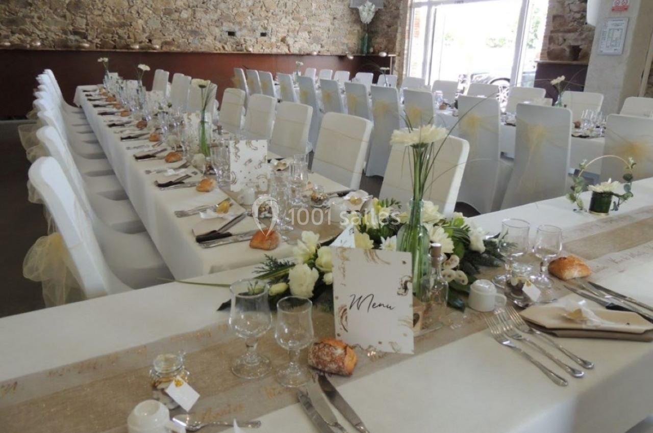 Salle de réception décorée pour un mariage avec longues tables dressées, nappes blanches et arrangements floraux.