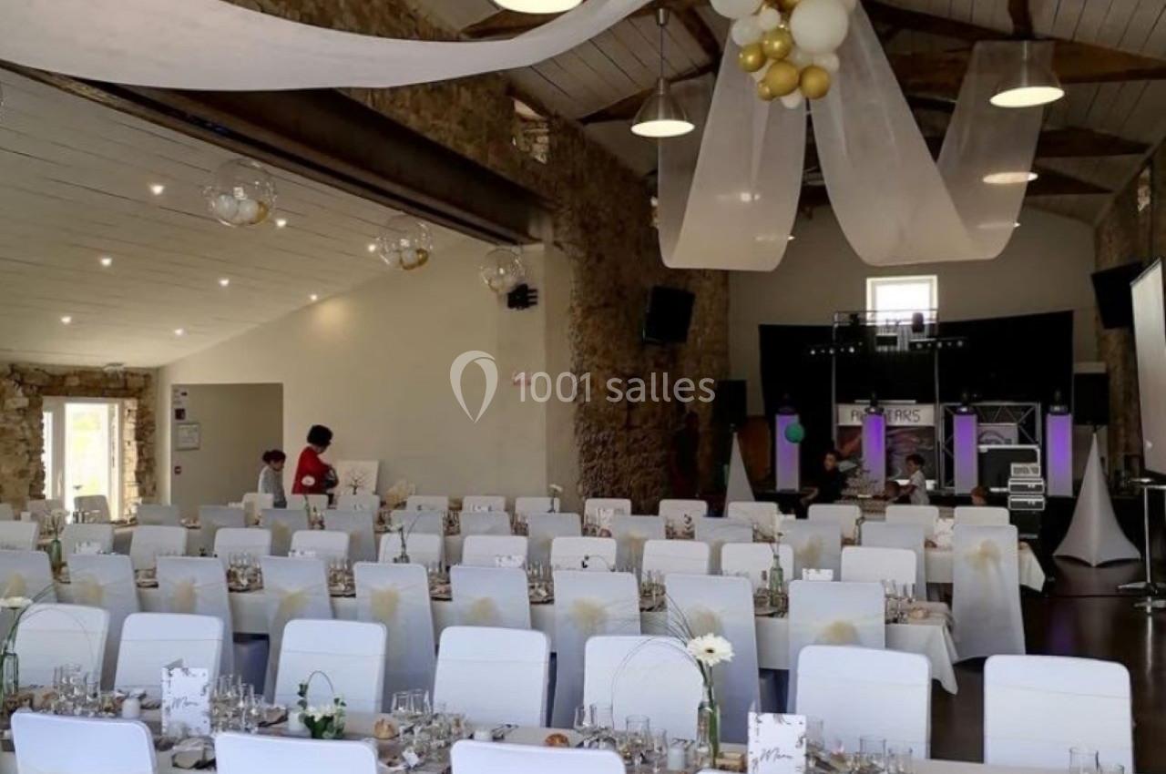 Salle de réception décorée avec des chaises blanches, des nœuds dorés, des tables dressées et des guirlandes suspendues.