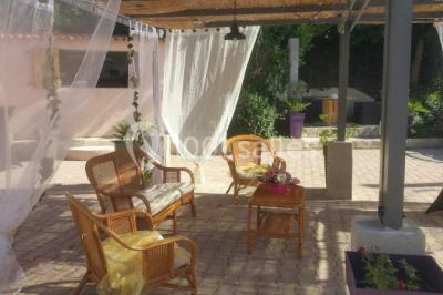 Salon de jardin en rotin avec coussins clairs, table basse décorée de fleurs, sur un sol pavé en extérieur.