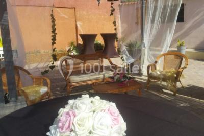 Salon de jardin en rotin avec coussins clairs, table basse décorée de fleurs, sur un sol pavé en extérieur.