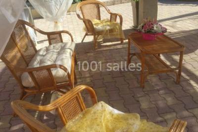 Salon de jardin en rotin avec coussins clairs, table basse décorée de fleurs, sur un sol pavé en extérieur.