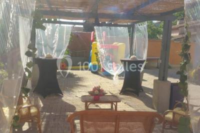 Salon de jardin en rotin avec coussins clairs, table basse décorée de fleurs, sur un sol pavé en extérieur.