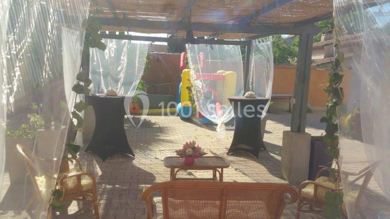 Espace extérieur avec pergola, mobilier en rotin et structure gonflable colorée en arrière-plan.