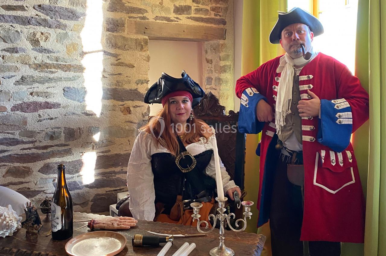 Deux personnes en costumes de pirates posent dans une pièce en pierre avec une table décorée d'objets anciens.