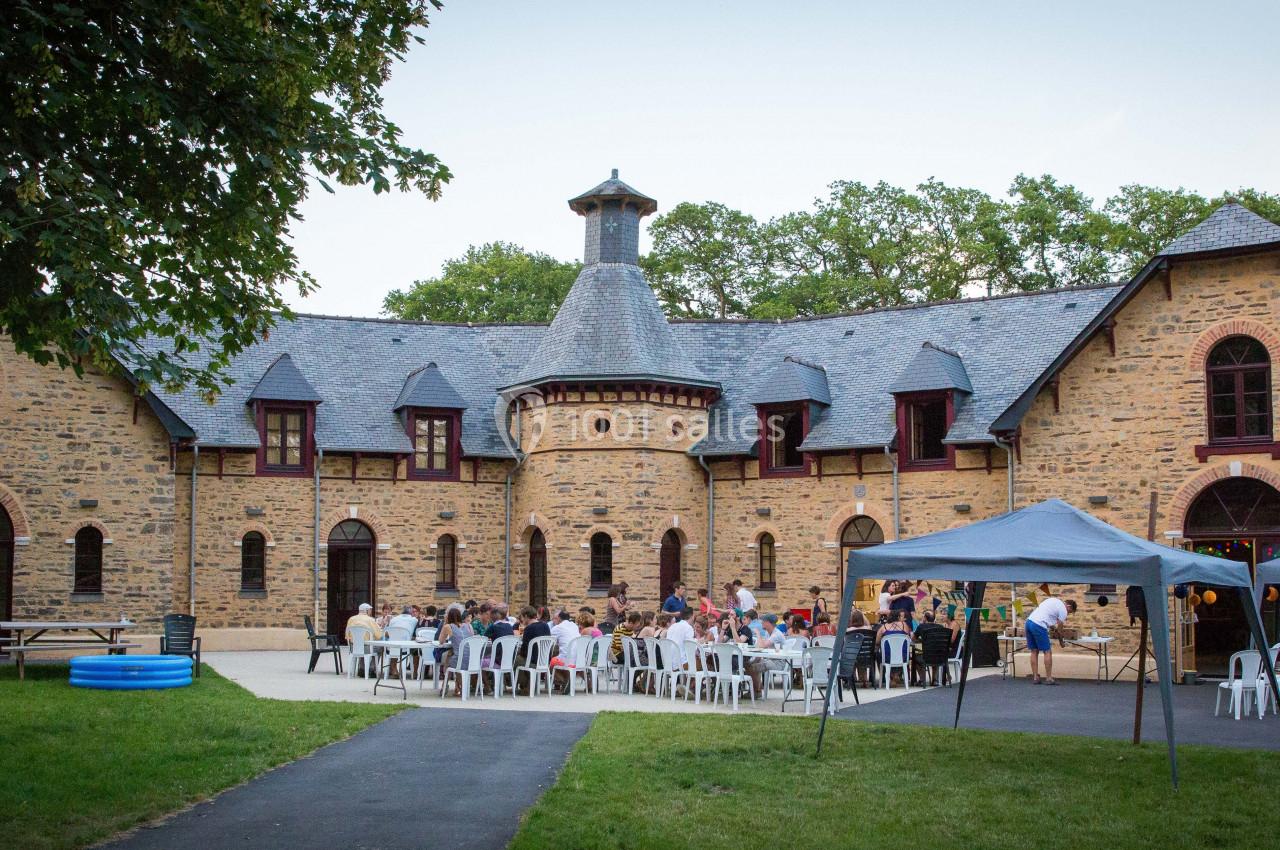 Groupe de personnes assises à l'extérieur devant un bâtiment en pierre avec des tentes et des arbres en arrière-plan.
