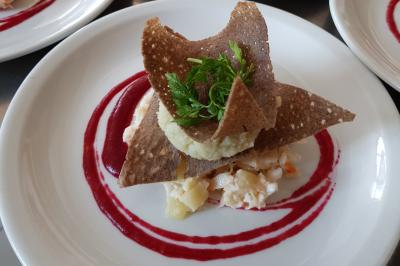 Cabane en bois perchée dans les arbres, entourée de forêt et bordée d'une prairie verdoyante.