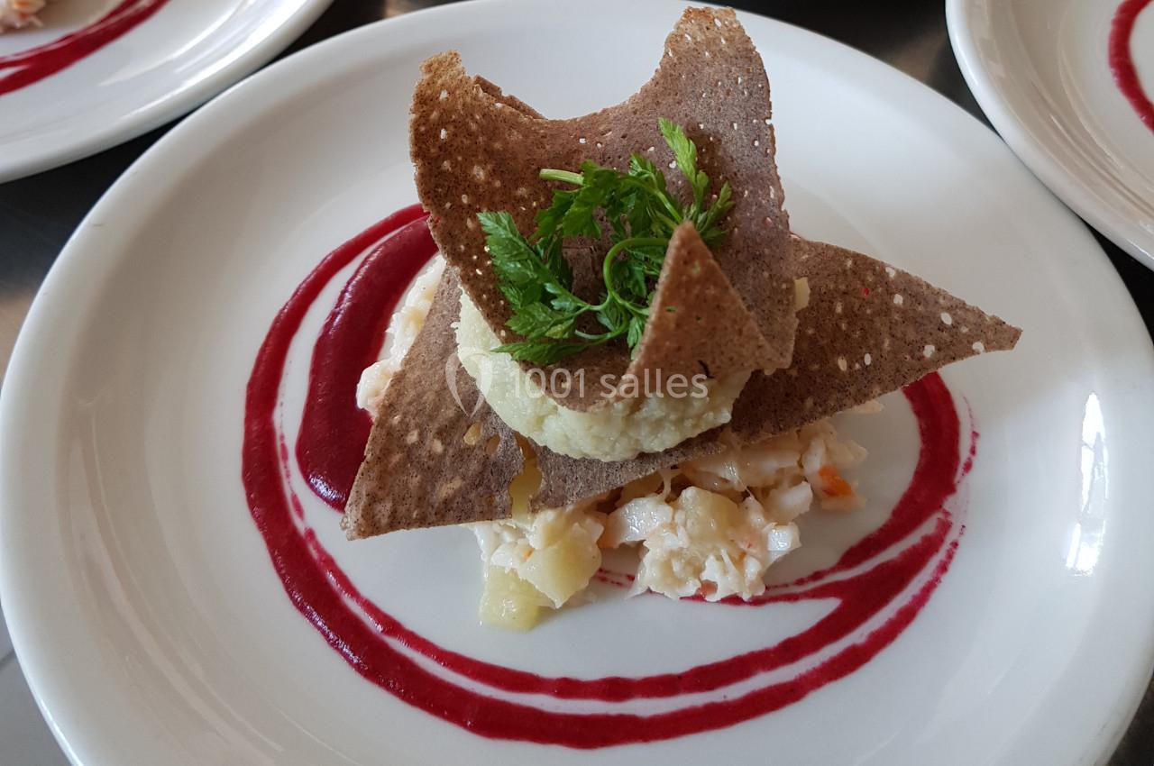 Assiette gastronomique avec tartare de poisson, chips croustillantes, purée et sauce rouge en décoration.