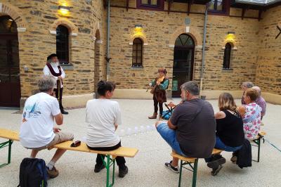 Cabane en bois perchée dans les arbres, entourée de forêt et bordée d'une prairie verdoyante.