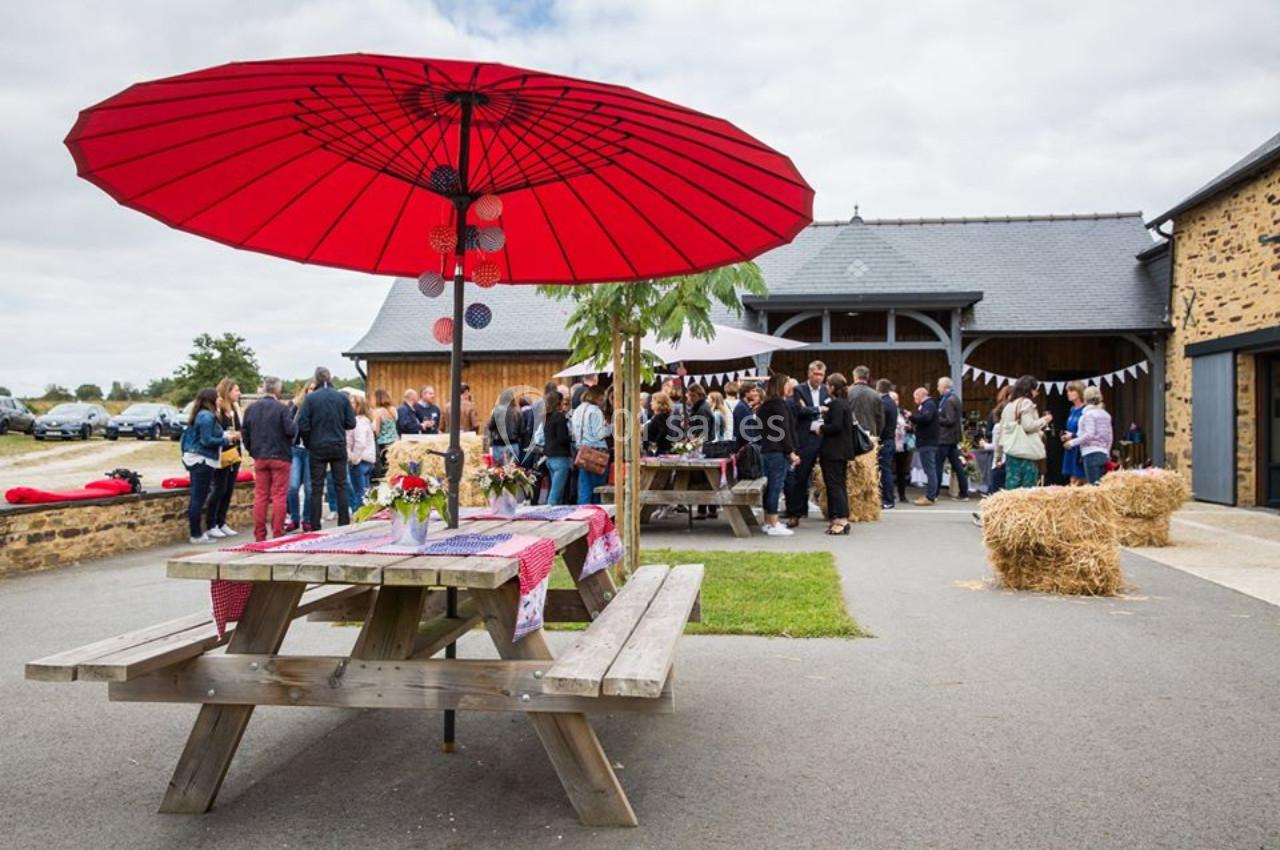 Groupe de personnes rassemblées devant un bâtiment en pierre, avec une table de pique-nique et un grand parasol rouge au…