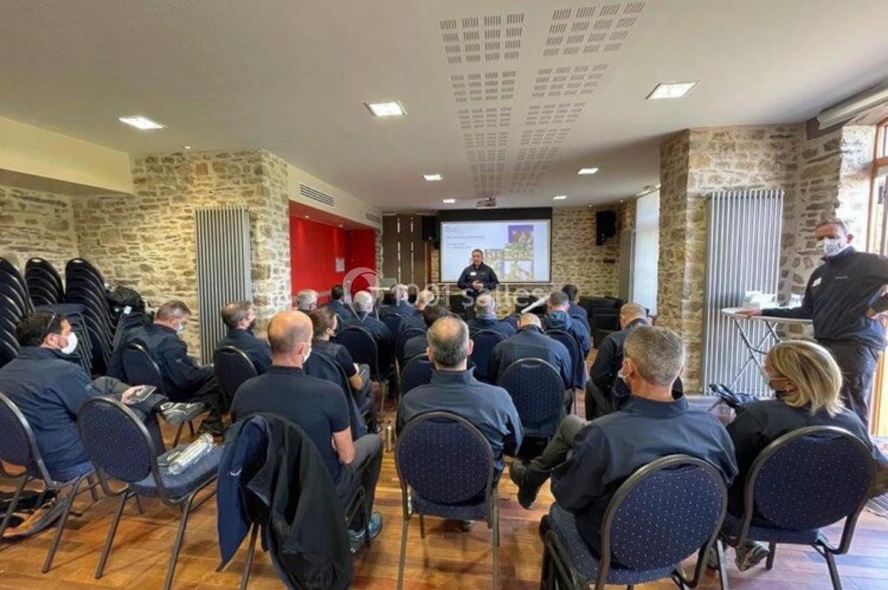 Un groupe de personnes assises dans une salle de réunion en pierre, écoutant un intervenant devant un écran de projection.