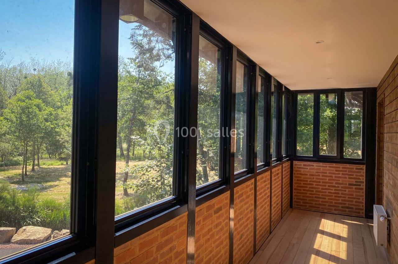 Véranda lumineuse avec murs en briques, grandes baies vitrées noires et vue sur un jardin verdoyant.