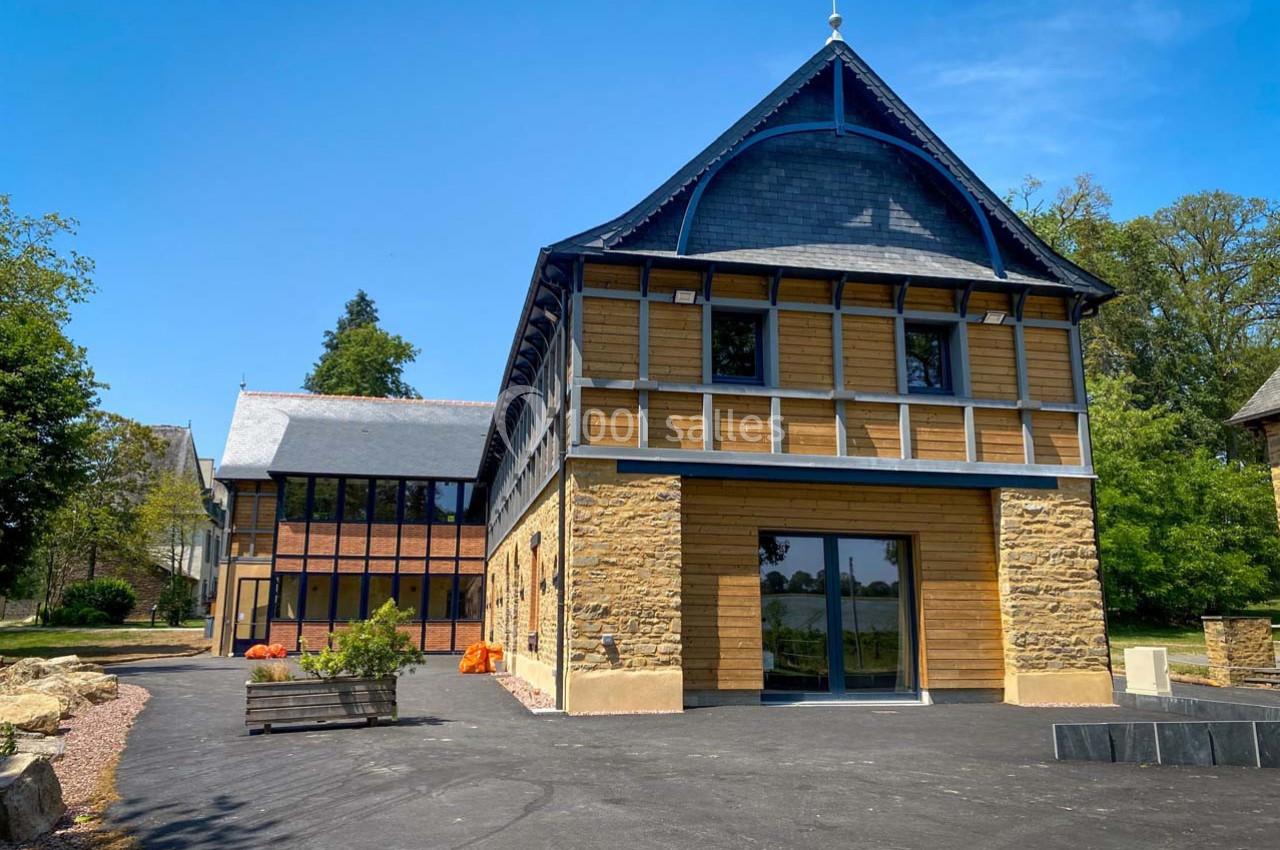 Bâtiment rénové en pierre et bois avec grandes baies vitrées, entouré de végétation sous un ciel bleu.
