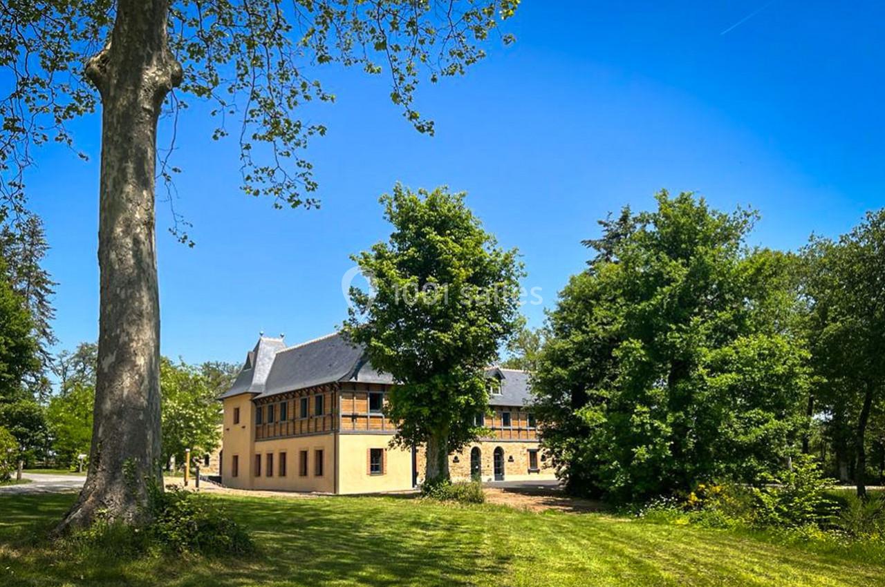 Bâtiment jaune à deux étages entouré d'arbres et d'une pelouse, sous un ciel bleu dégagé.