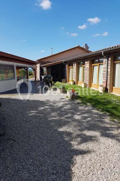 Allée en gravier bordée de pelouse menant à une maison en briques avec de grandes baies vitrées sous un ciel bleu.