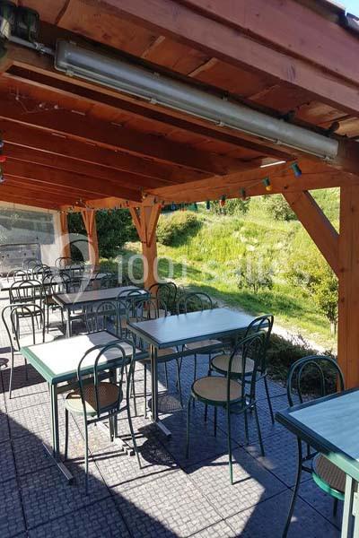 Terrasse couverte avec des tables et chaises en métal, située dans un environnement verdoyant.