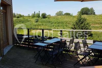Tables hautes recouvertes de nappes blanches, décorées de bouquets, dans une salle lumineuse avec baies vitrées.