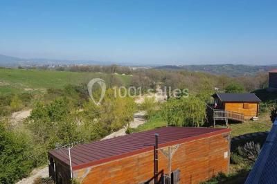 Tables hautes recouvertes de nappes blanches, décorées de bouquets, dans une salle lumineuse avec baies vitrées.