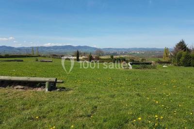 Tables hautes recouvertes de nappes blanches, décorées de bouquets, dans une salle lumineuse avec baies vitrées.