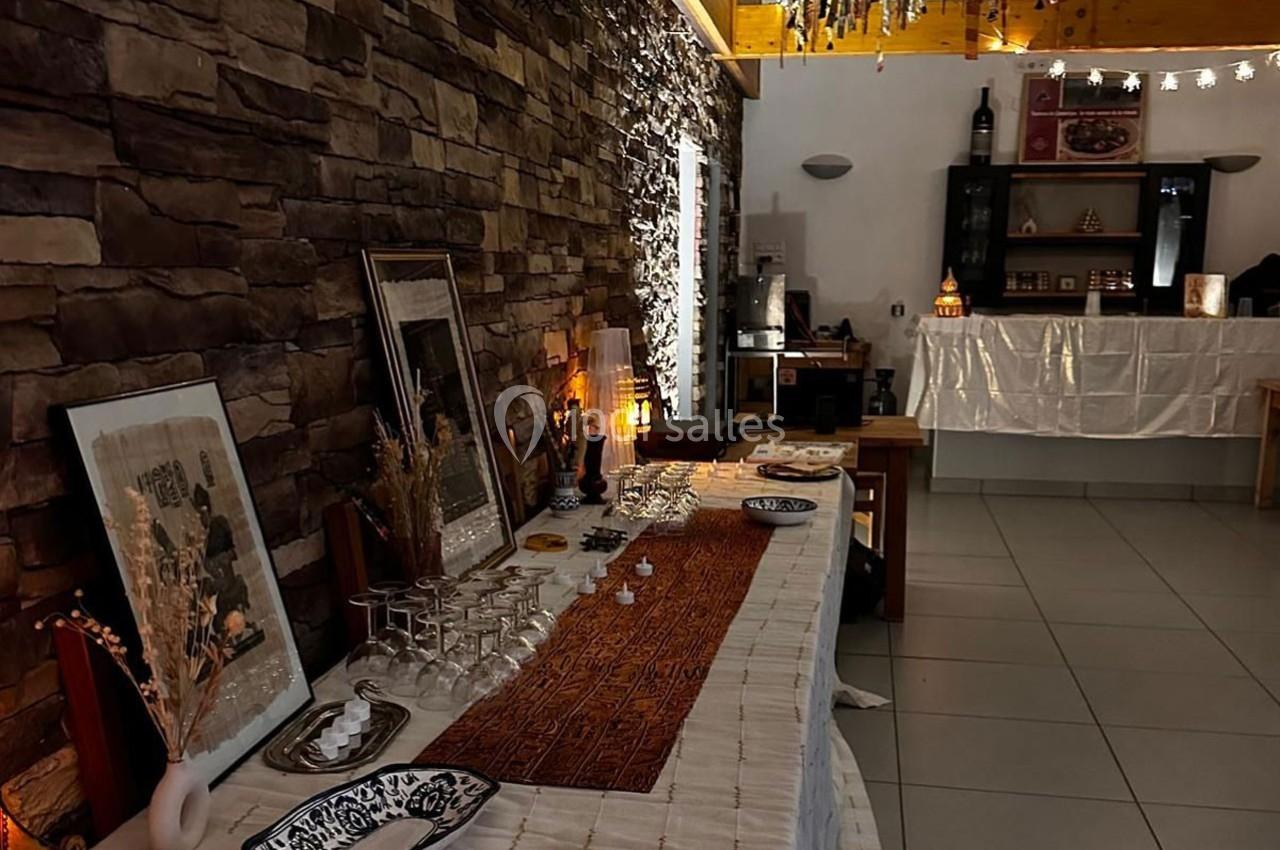 Table décorée avec des objets artisanaux, nappes et vaisselle, dans une pièce éclairée avec des murs en pierre.