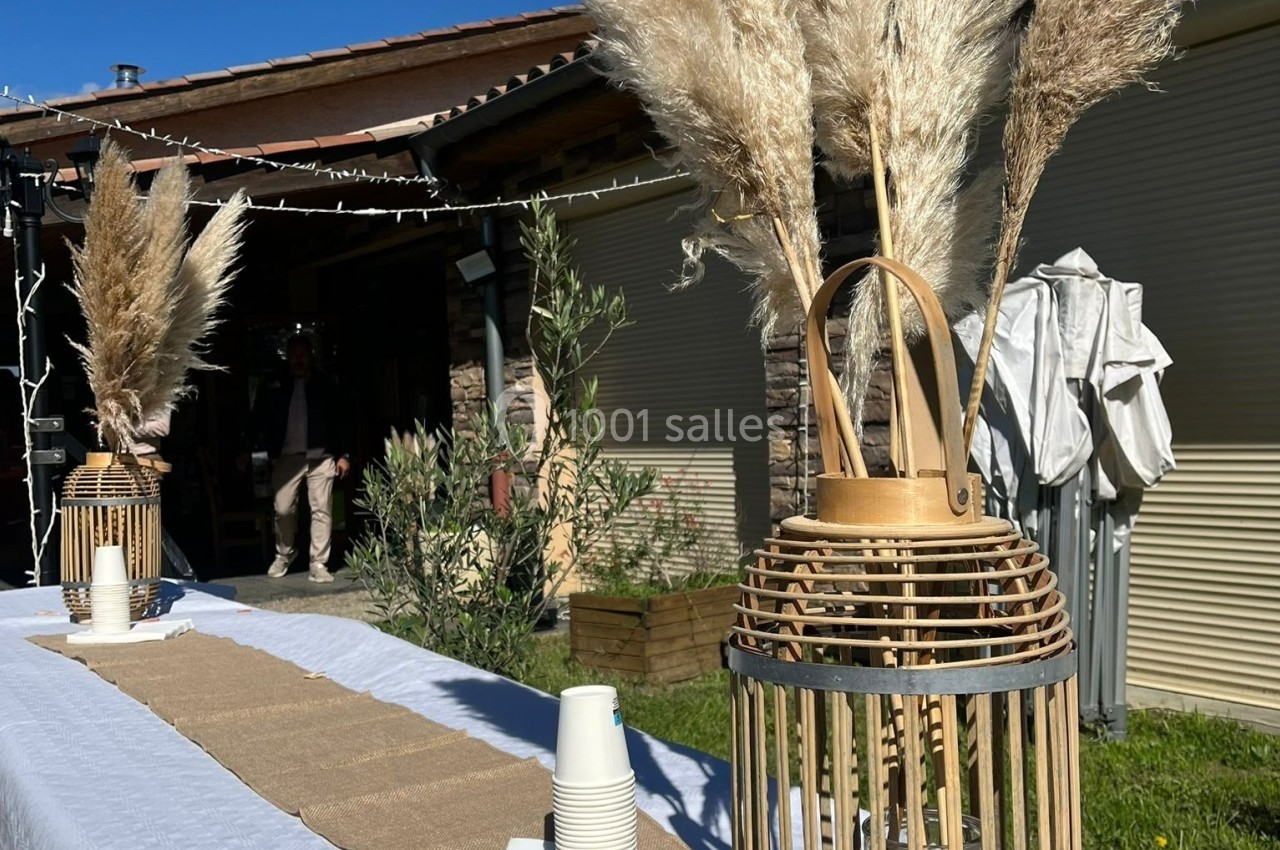 Deux lanternes en bois avec des bouquets de pampas décorent une table extérieure sous un ciel ensoleillé.