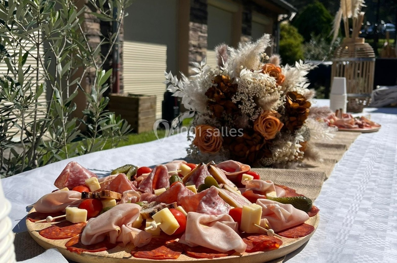 Plateau de charcuterie et fromages sur une table décorée, avec un bouquet de fleurs séchées en arrière-plan.