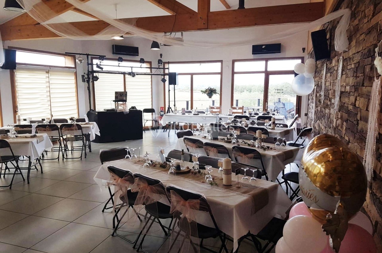 Salle de réception décorée pour un événement, avec tables dressées, chaises ornées de nœuds roses et ballons festifs.