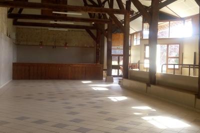 Grande salle lumineuse avec charpente en bois apparente, sol carrelé et murs clairs, éclairée par des fenêtres.