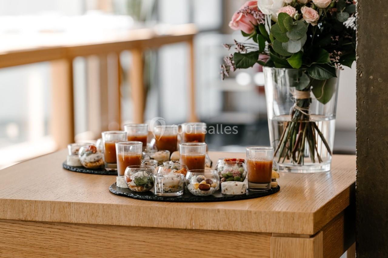 Plateau de verrines salées et sucrées disposé sur une table en bois, avec un vase de fleurs en arrière-plan.