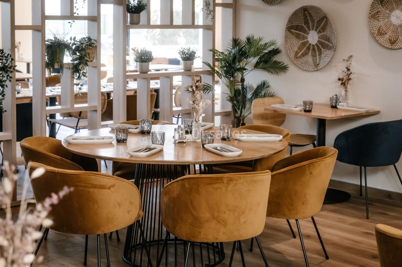 Salle de restaurant moderne avec table ronde, chaises en velours jaune et décorations murales en osier.