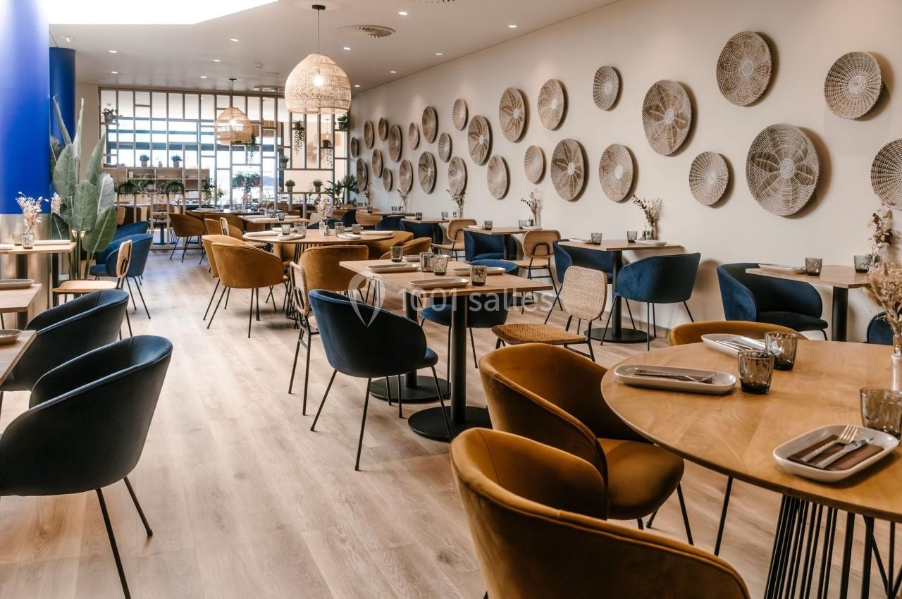 Salle de restaurant moderne avec tables en bois, chaises colorées et décor mural composé de paniers tressés.
