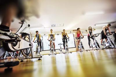 Personnes faisant du vélo d'intérieur en groupe dans une salle de sport lumineuse.