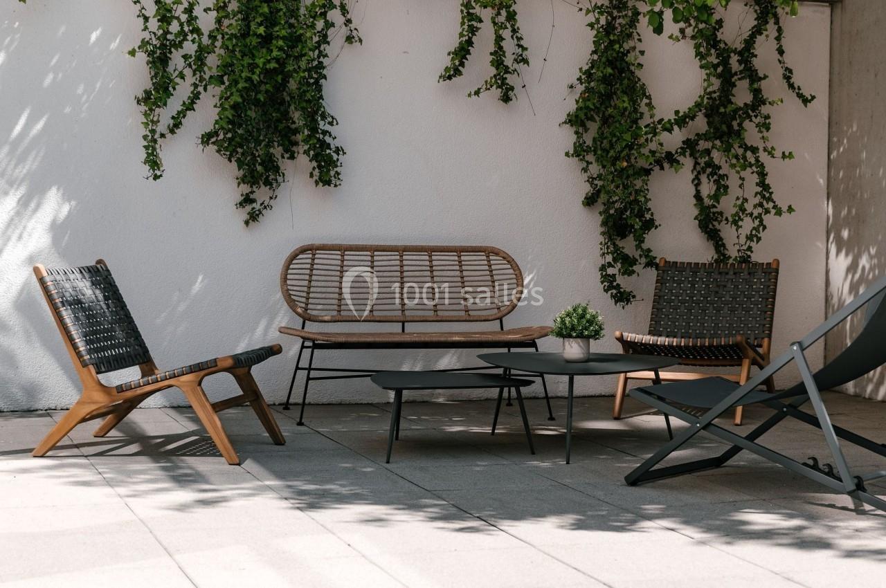 Mobilier de jardin en bois et rotin avec table basse, disposé sur une terrasse ensoleillée, entourée de plantes grimpantes.