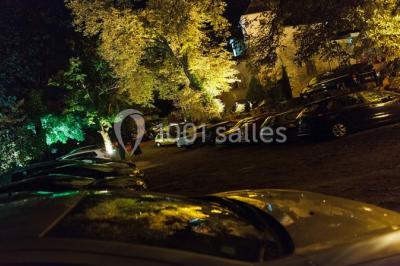 Parking extérieur de nuit, éclairé par des lumières jaunes et entouré d'arbres et de bâtiments.
