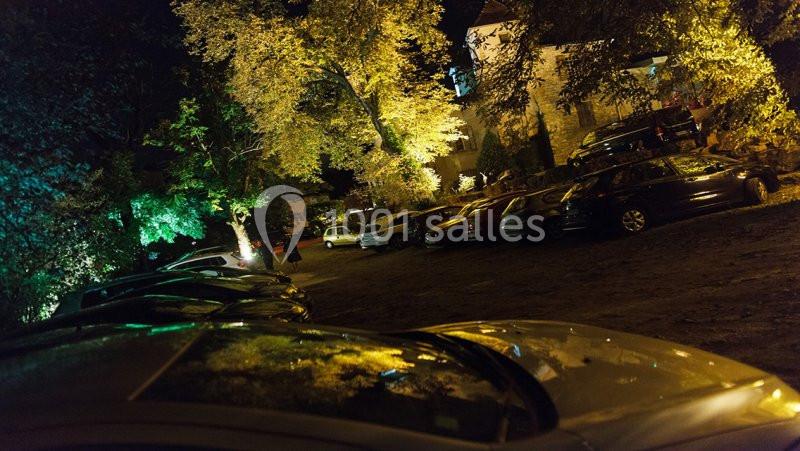 Parking extérieur de nuit, éclairé par des lumières jaunes et entouré d'arbres et de bâtiments.