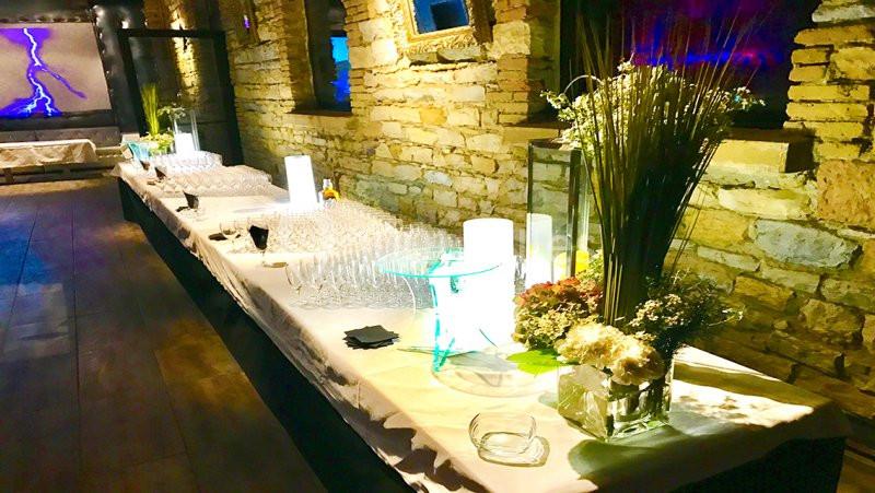 Table décorée avec des fleurs, verres alignés et éclairages doux dans une salle aux murs en pierre apparente.